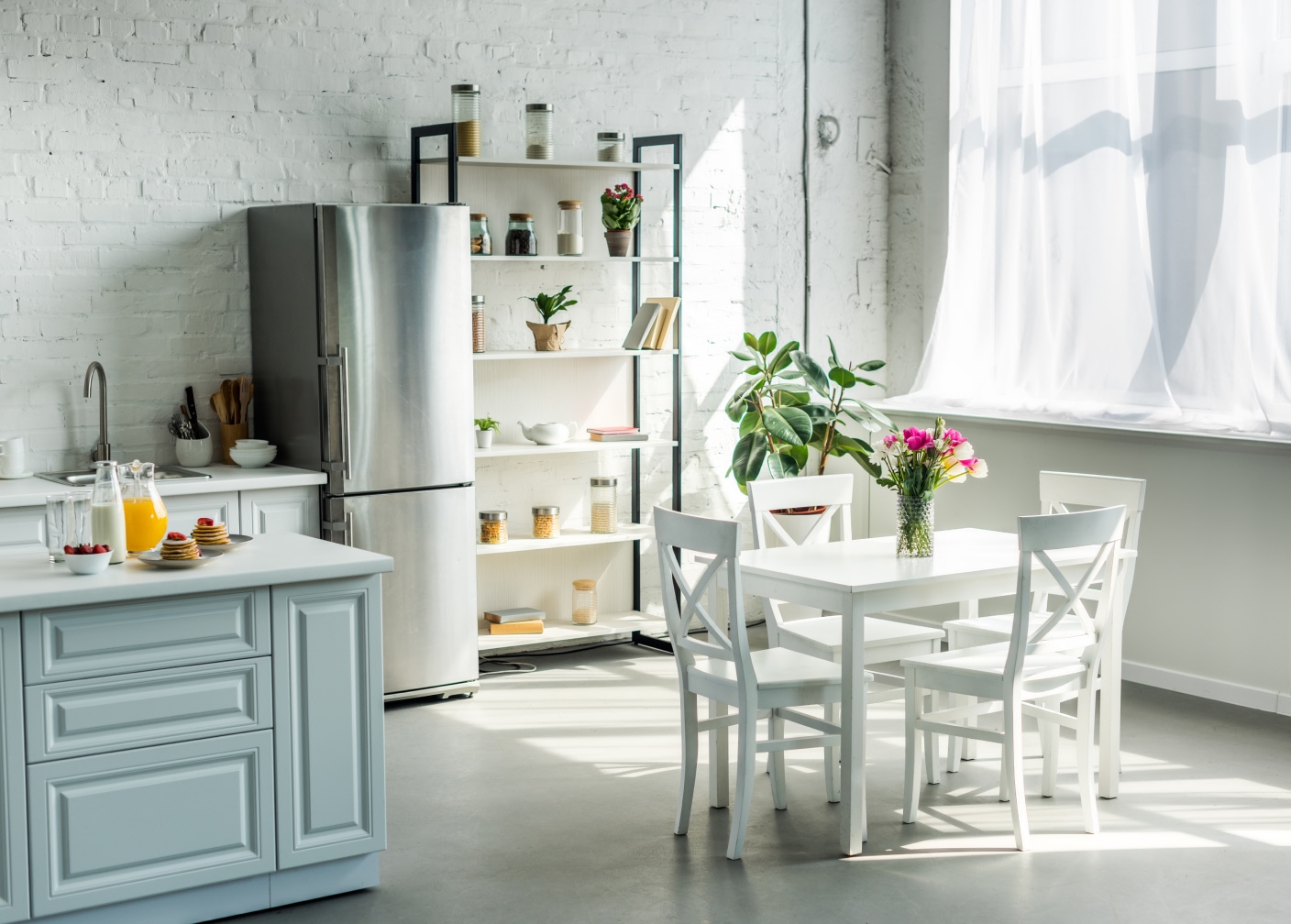 Ljust och städat kök med vitt matbord, stolar och blommor vid fönstret